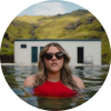 Mujer con traje de baño rojo y gafas de sol disfrutando de una piscina de aguas termales naturales en Islandia.