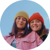 Dos mujeres jóvenes con sombreros coloridos sonriendo al aire libre.
