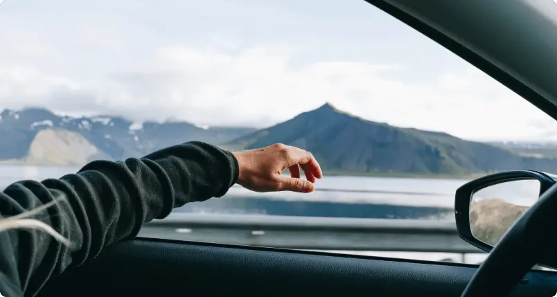 Una mano asomándose por la ventana de un coche mientras conduce a través de los impresionantes paisajes de Islandia, representando la asistencia en carretera confiable de Cars Iceland para un viaje sin preocupaciones.