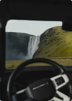 Vista de la cascada Skógafoss a través del parabrisas de un auto en Islandia, capturando la icónica cascada enmarcada por el volante del vehículo.