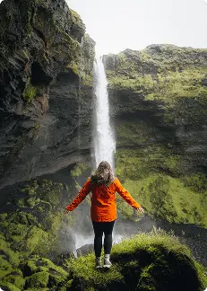 Viajero con chaqueta naranja frente a una cascada islandesa, conectando con la naturaleza y la aventura en el corazón de Islandia.
