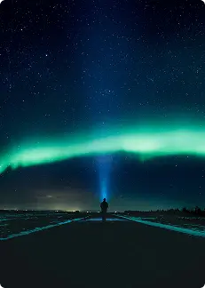 Silueta de una persona con una linterna bajo las auroras boreales en Islandia, iluminando el cielo nocturno lleno de estrellas.