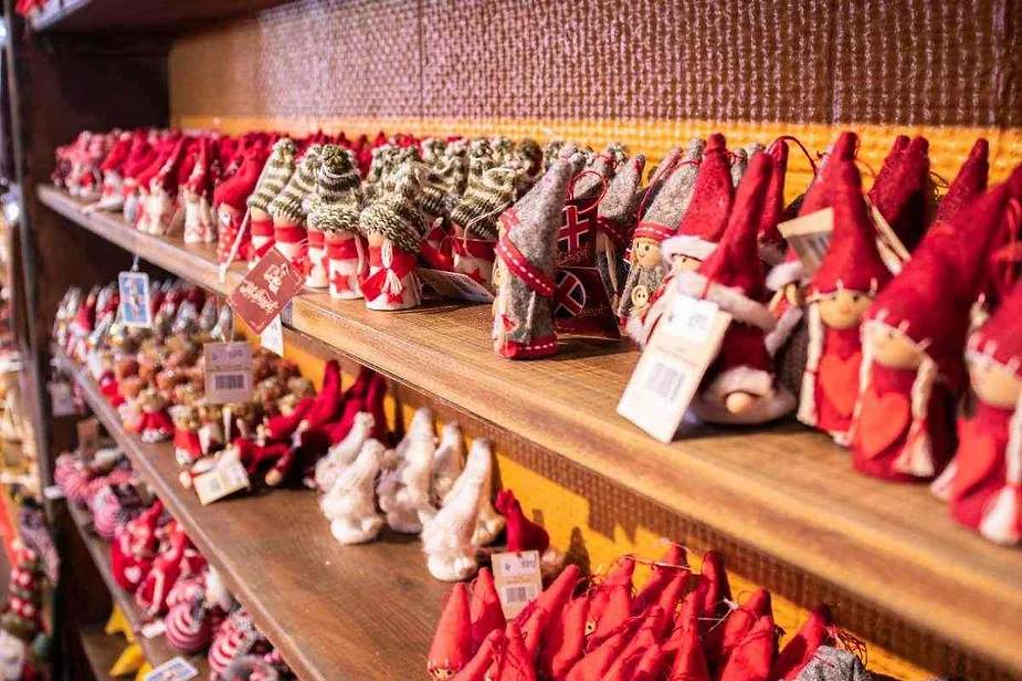 Estantes llenos de una variedad de decoraciones navide&ntilde;as hechas a mano, incluidos gnomos, adornos y figuras festivas, todos adornados con los tradicionales colores festivos rojo, blanco y verde.