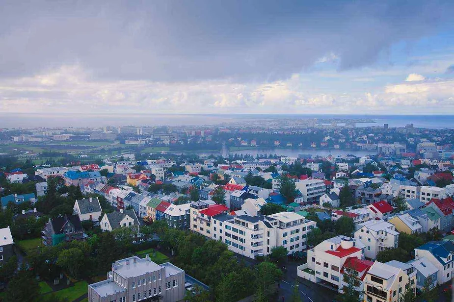 Vista aérea de Reykjavik, Islandia, que muestra tejados coloridos, una mezcla de edificios tradicionales y modernos, con la costa y el océano visibles en la distancia bajo un cielo nublado.