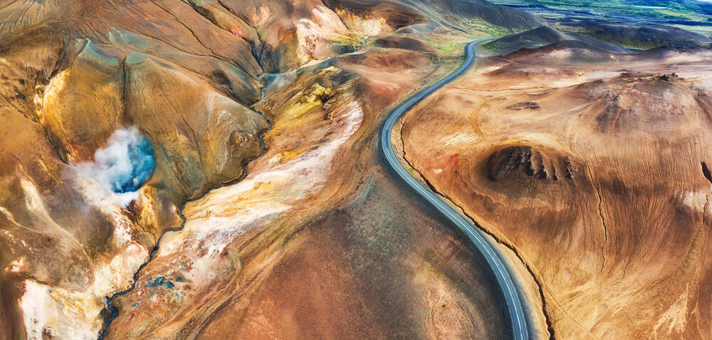 Un coche circula por una carretera panorámica de Islandia al atardecer, rodeado de campos verdes y montañas a lo lejos.