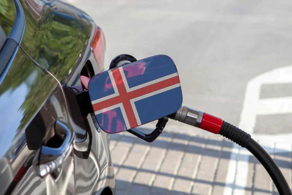 Coche repostando en una gasolinera con la bandera islandesa en el tapón del depósito, que representa los viajes y el transporte en Islandia.