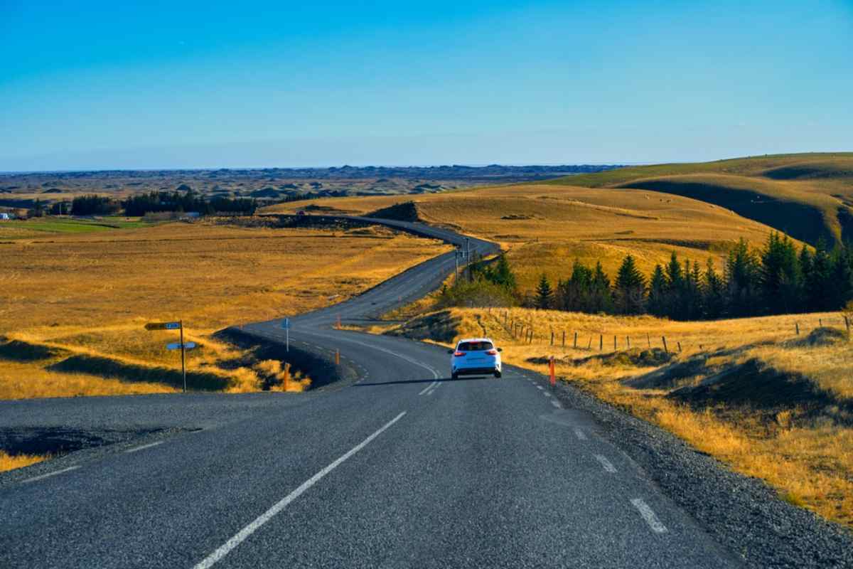Coche de alquiler blanco conduciendo por una carretera asfaltada vacía a través de campos dorados y colinas onduladas en Islandia.