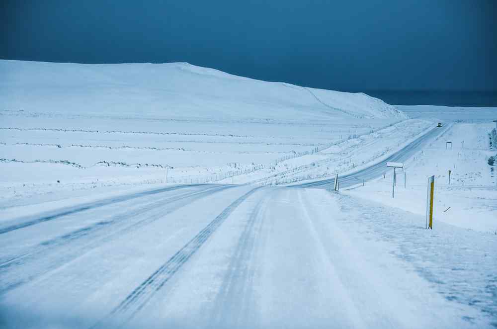 Carretera rural helada que atraviesa un paisaje islandés cubierto de nieve bajo un cielo oscuro.