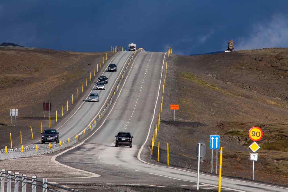 Coches circulando por la Ruta 1 de Islandia junto a una señal de límite de velocidad de 90 km/h en un remoto paisaje volcánico.