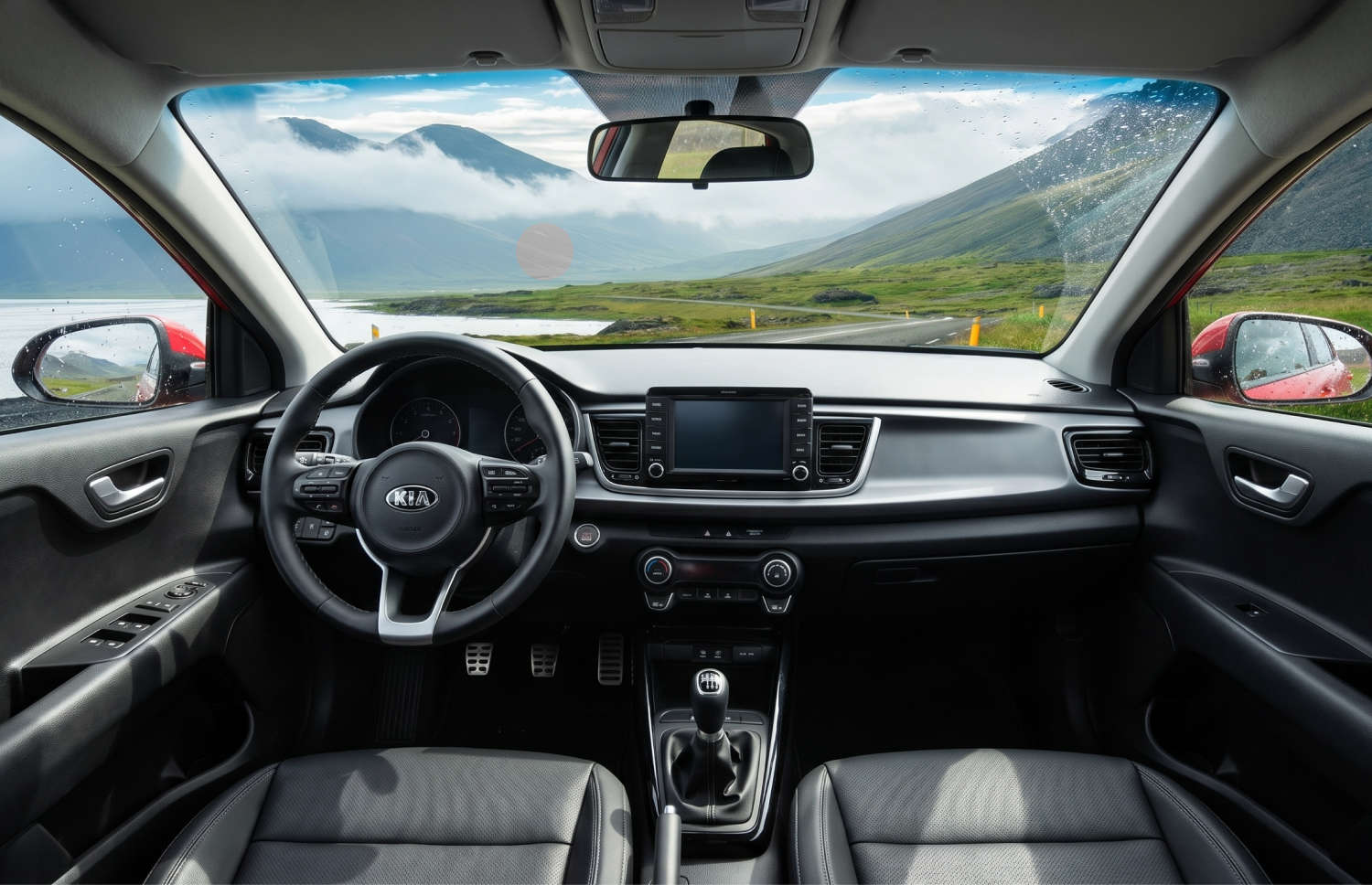 Kia Rio azul con transmisión manual, GPS, cámara de reversa y espacio para 5 pasajeros y 2 maletas, ideal para viajes por carretera en Islandia.